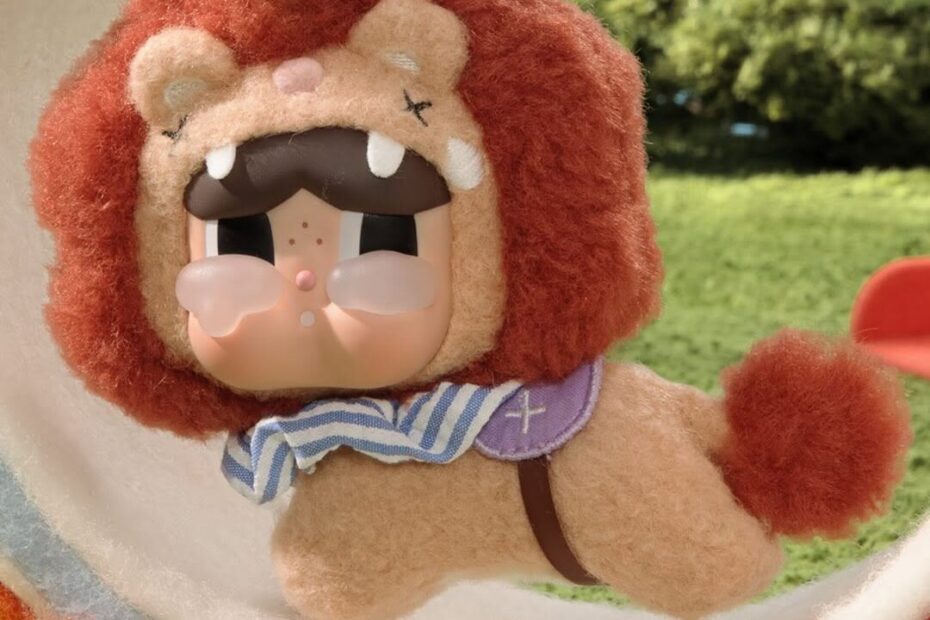 CRYBABY dressed as a lion with a gold crown and striped scarf, leaping through a striped hoop